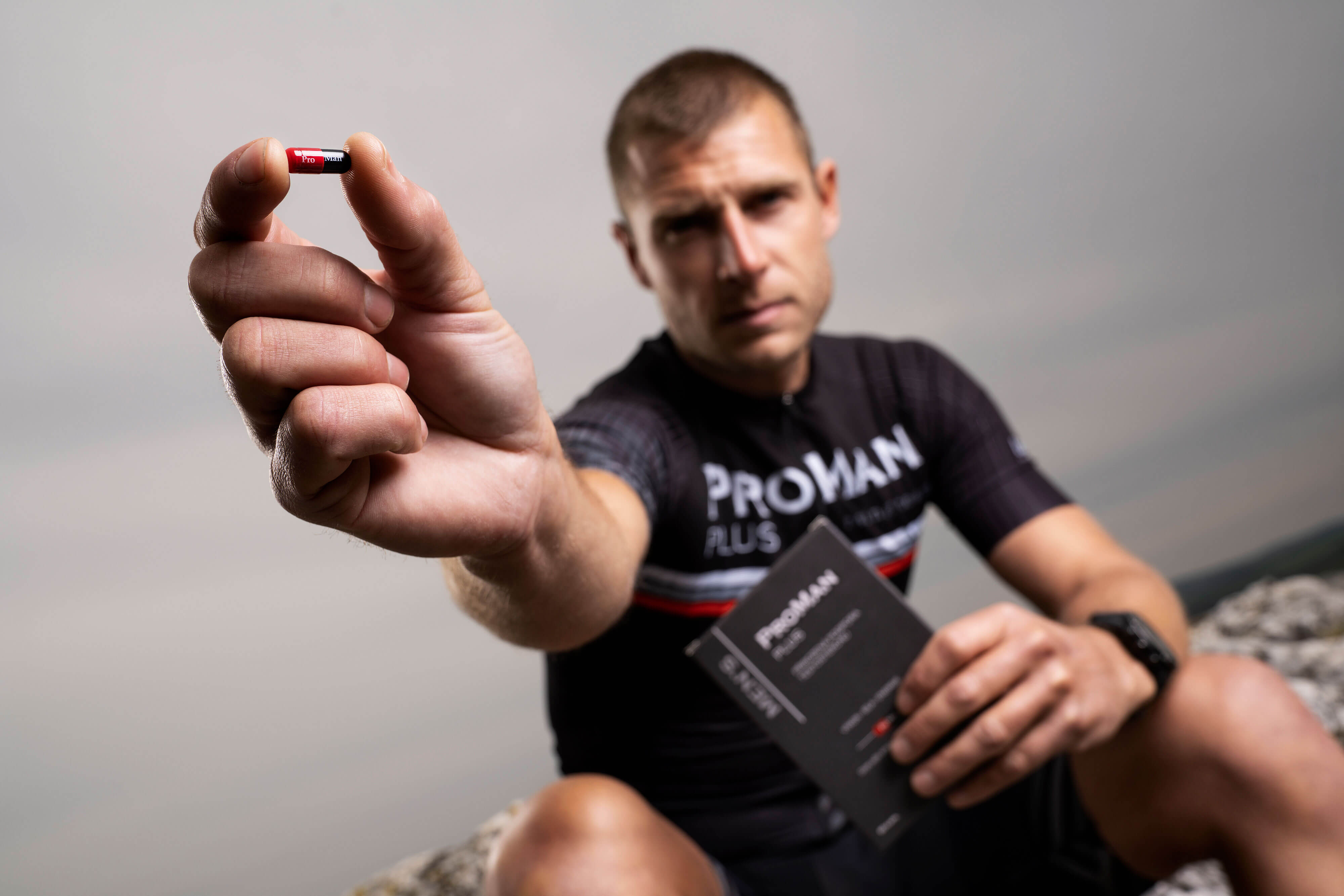 Natural Pharmaceuticals ProMan® Plus Egy sportruházatot viselő férfi kinyújtott kezében egy ProMan® Plus étrend-kiegészítő kapszulát tart.